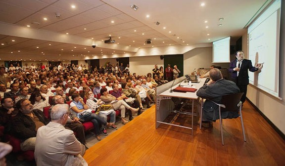 Foto esquerra: Santiago Niño Becerra a la conferència al Fòrum de Debats. Foto: Adrià Costa.